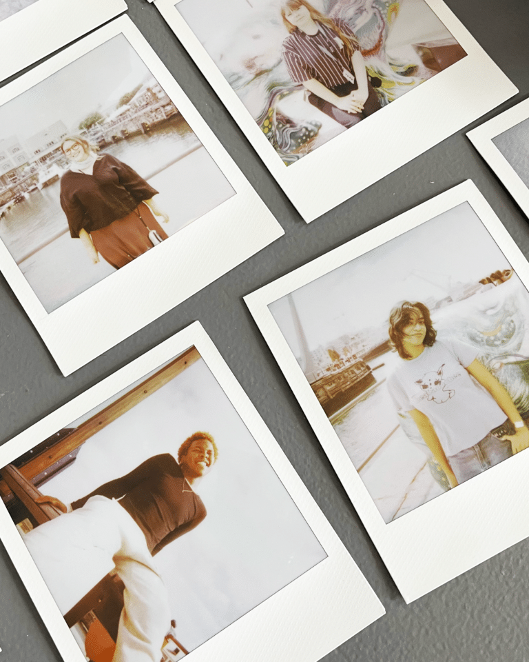 Several polaroid photo prints spread on a dark surface, each featuring people posing outdoors or by water in casual clothing.