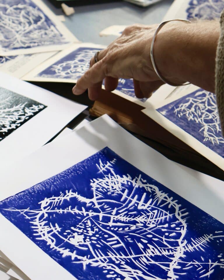 Close-up of a hand with a silver bracelet pointing at blue prints with white abstract lines and shapes laid on a table