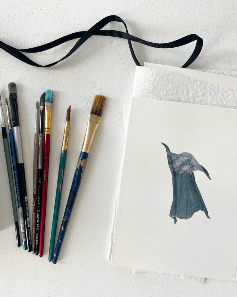 Assorted paintbrushes of varying sizes lined up on a white textured surface with masking tape and a printed image on the right side.