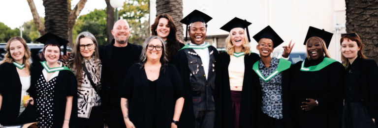 Group of diverse graduates in caps and gowns posing outdoors, smiling together.