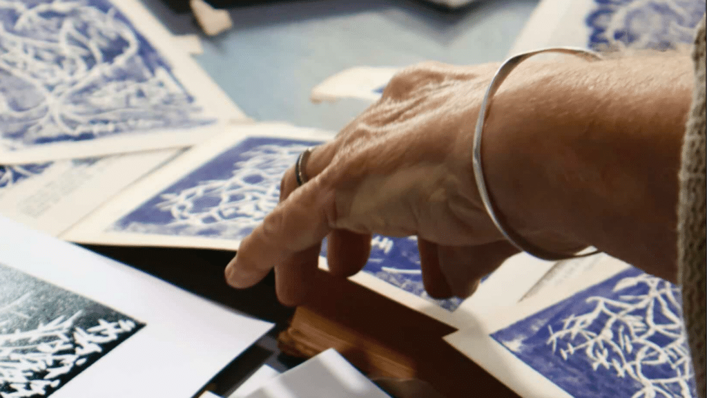 Close-up of a hand with a wedding band and bracelet, pointing at blue patterned cards on a table.
