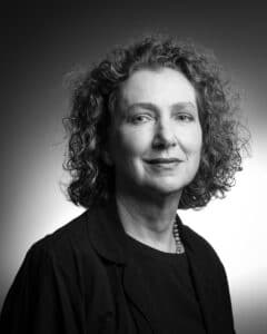 Black-and-white portrait of a smiling woman with curly hair, wearing a dark blouse and pearl necklace.